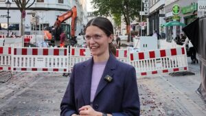 Annika Hanke-Wiedemann, Projektleiterin von freiRaum Ottensen, steht lächelnd vor Bauzäunen und einem Bagger auf einer Baustelle in Ottensen.